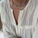 Picture of a woman wearing a white blouse and wearing 4 dainty bead necklaces in colors of white, blues, pinks and golds.