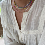 Picture of a woman wearing a white blouse and wearing 4 dainty bead necklaces in colors of white, blues, pinks and golds.
