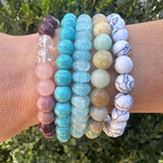 Multiple beaded bracelets in blues, pinks and whites on a wrist with a natural background