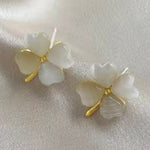 Pair of white floral earrings with gold accents on a light fabric background
