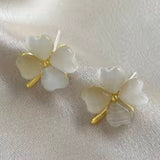 Pair of white floral earrings with gold accents on a light fabric background