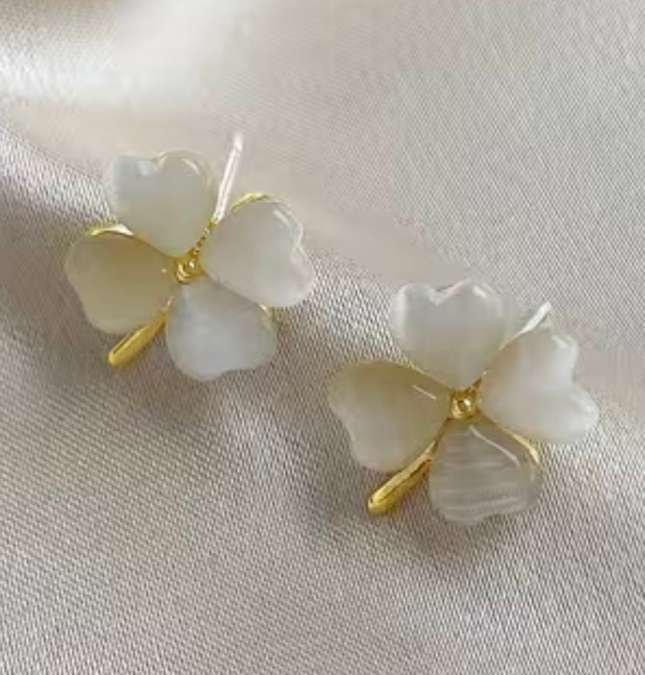Pair of white floral earrings with gold accents on a light fabric background