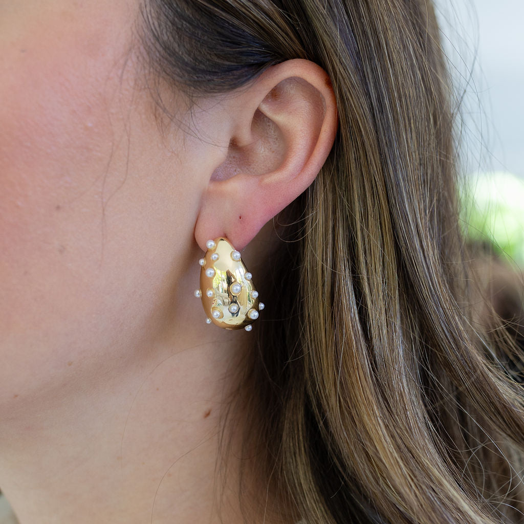 Woman wearing gold chunky teardrop earrings inlaid with small pearls.