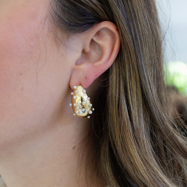 Woman wearing gold chunky teardrop earrings inlaid with small pearls.