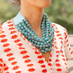 Woman outside wearing a white dress with a red lips print and a big blue stone layered necklace around her neck