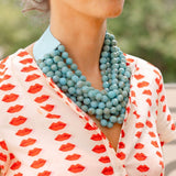 Woman outside wearing a white dress with a red lips print and a big blue stone layered necklace around her neck