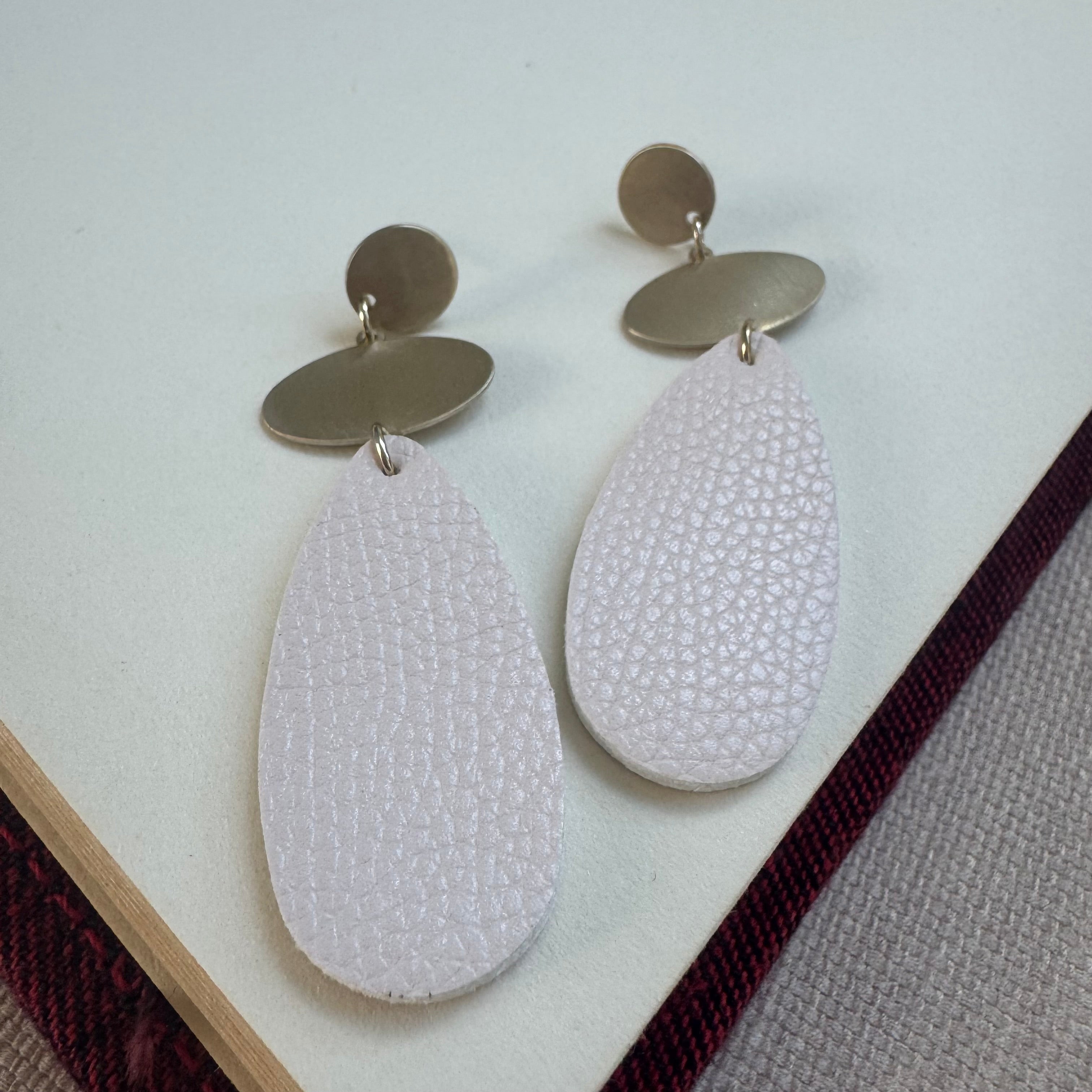 Gold and White dangle earrings. Earrings have a small gold circle base, a small oval and large white teardrop beads at the base.