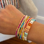 A person's wrist wearing multiple colorful beaded bracelets in various colors.