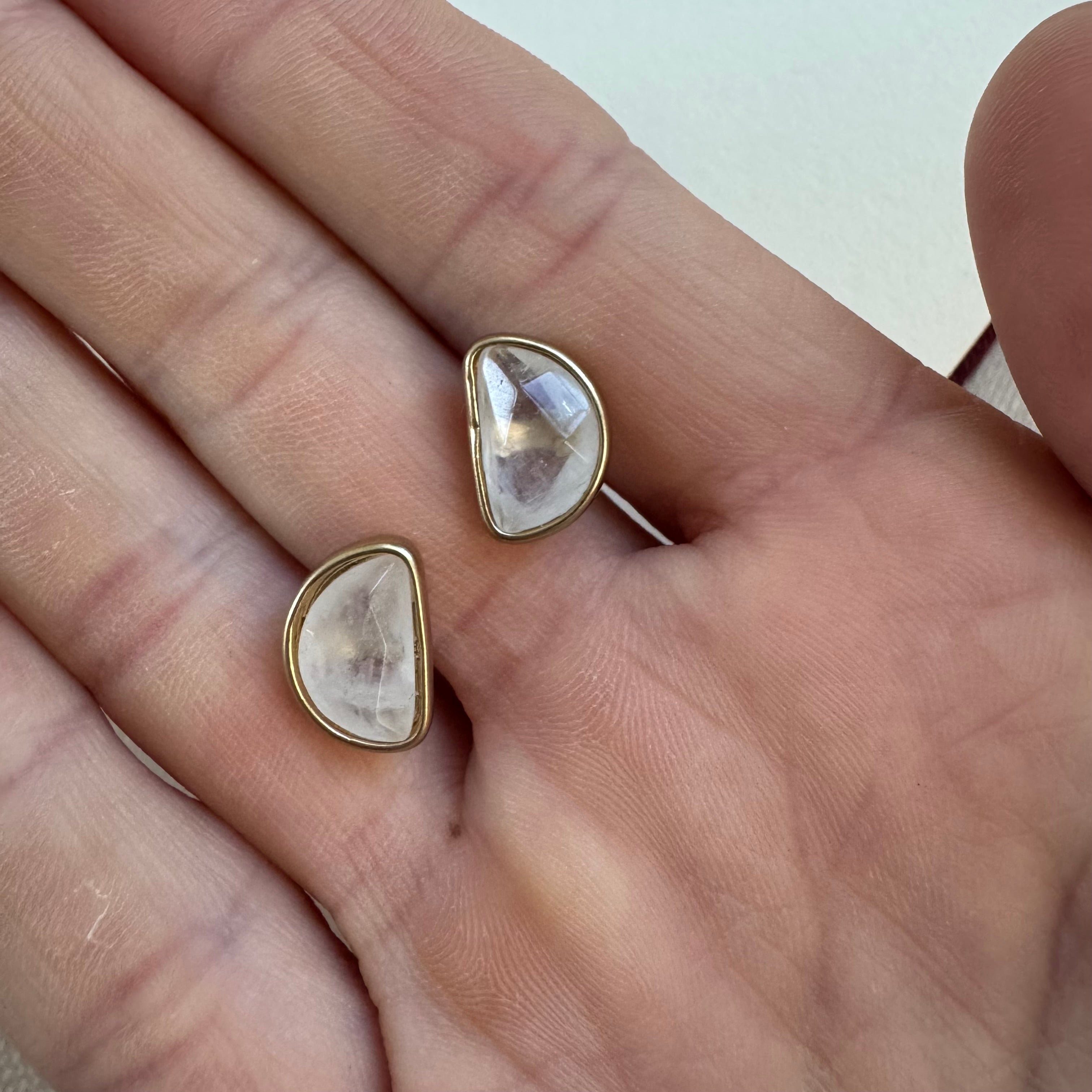 Picture of a hand holding clear stone half moon Studs in a gold setting.