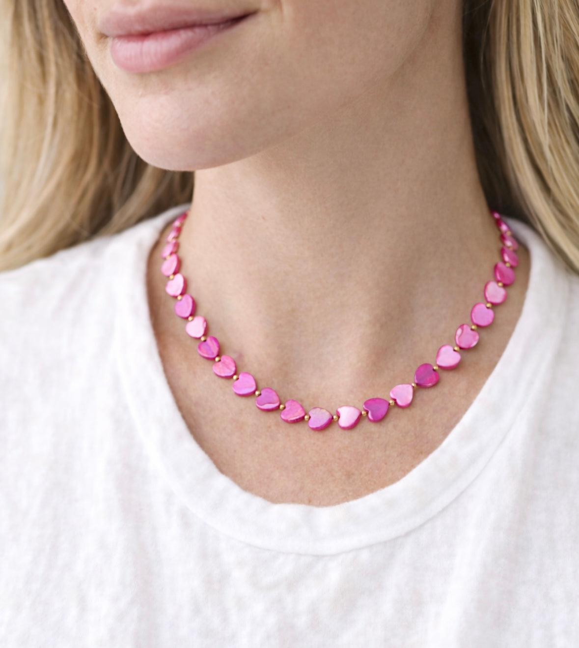 Close-up of a person wearing a pink heart-shaped beaded necklace on a white background