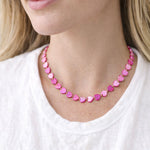 Close-up of a person wearing a pink heart-shaped beaded necklace on a white background