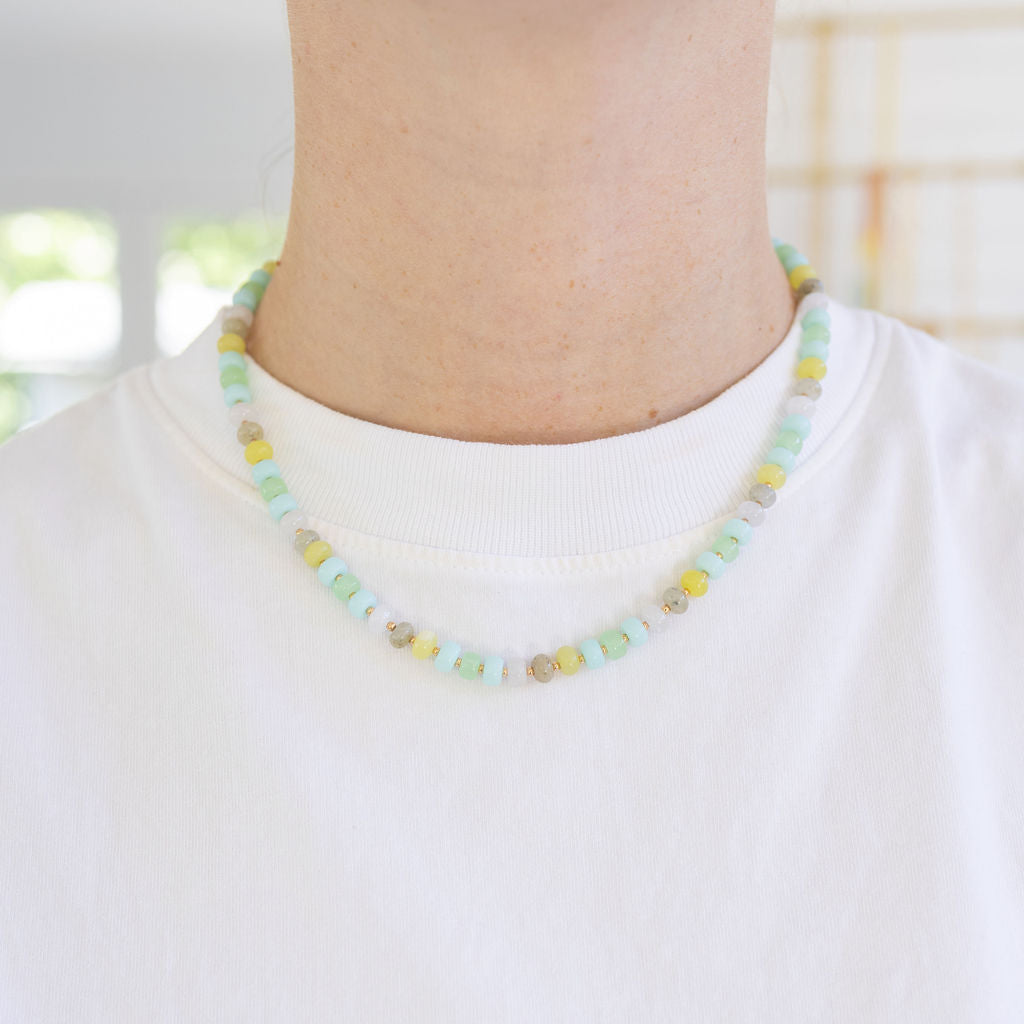 Picture of a woman's neck displaying a small bead necklace in colors of light greens, yellows and light blues.