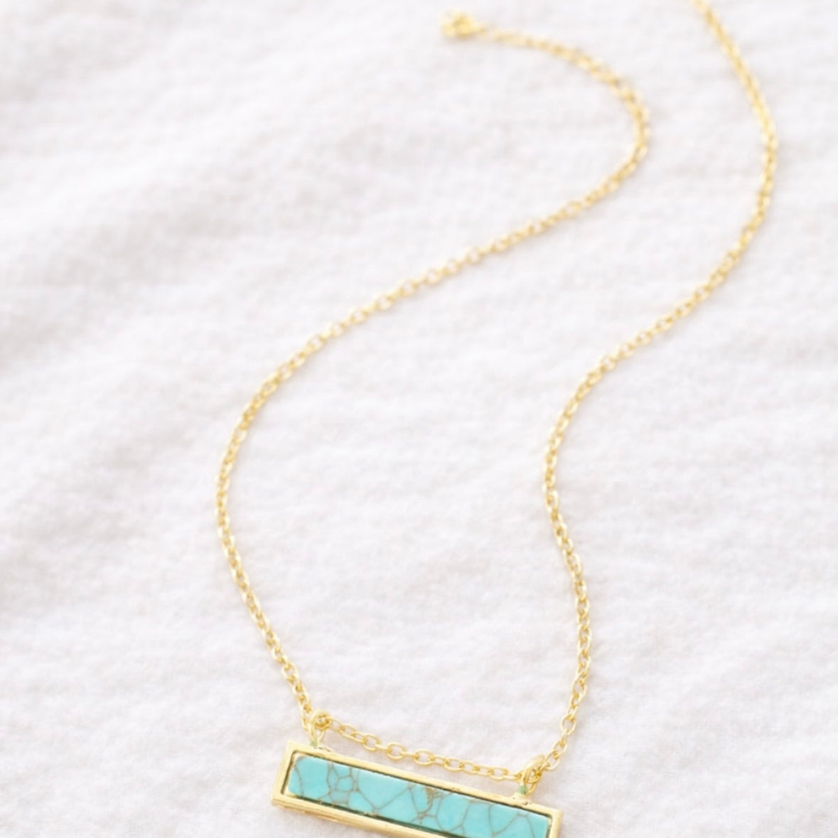 Gold necklace with a turquoise bar pendant on a white background