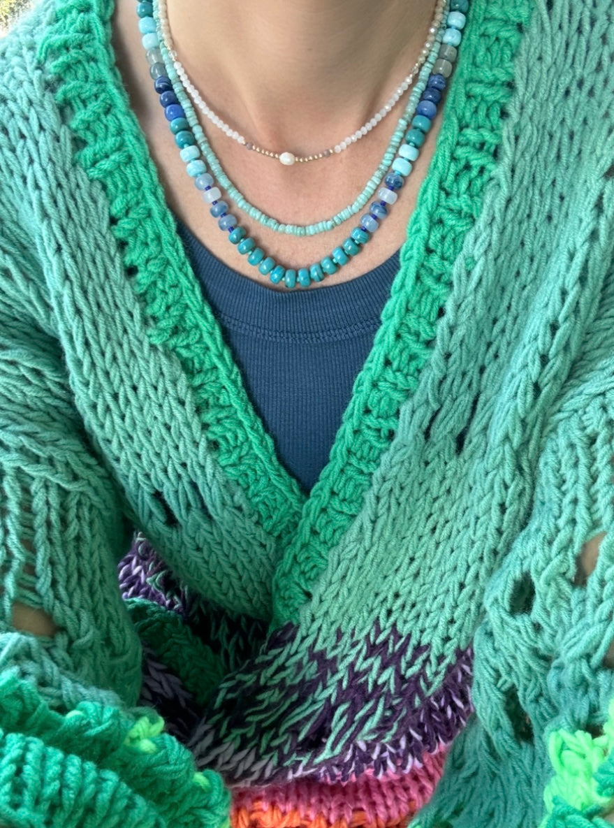 Picture of the front of a woman wearing a set of three bead necklaces. Necklace beads are blues and turquoise