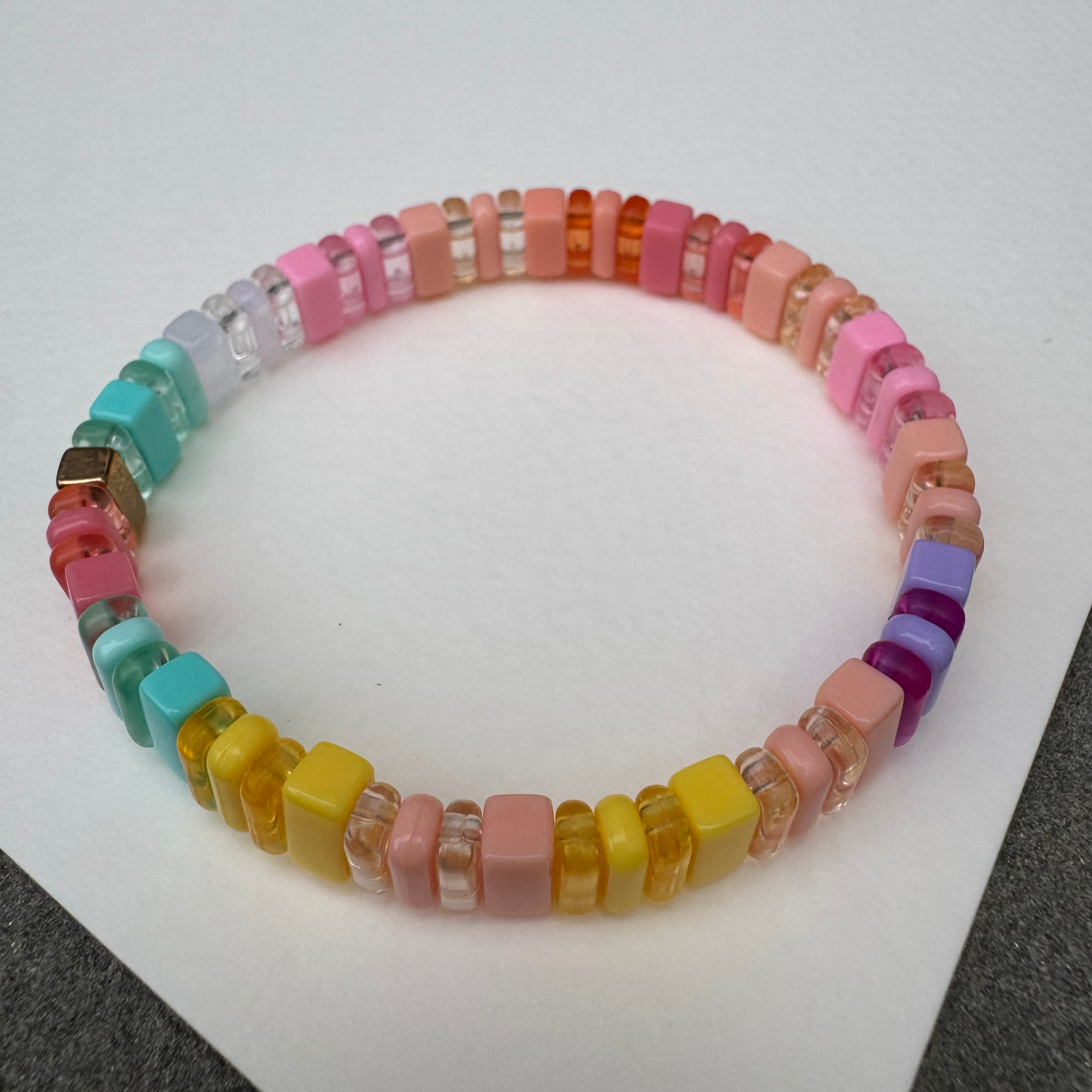 Picture of a multicolored bead bracelet. Bracelet is made up of matte and clear yellow, peach, coral, pink, turquoise and purple beads.