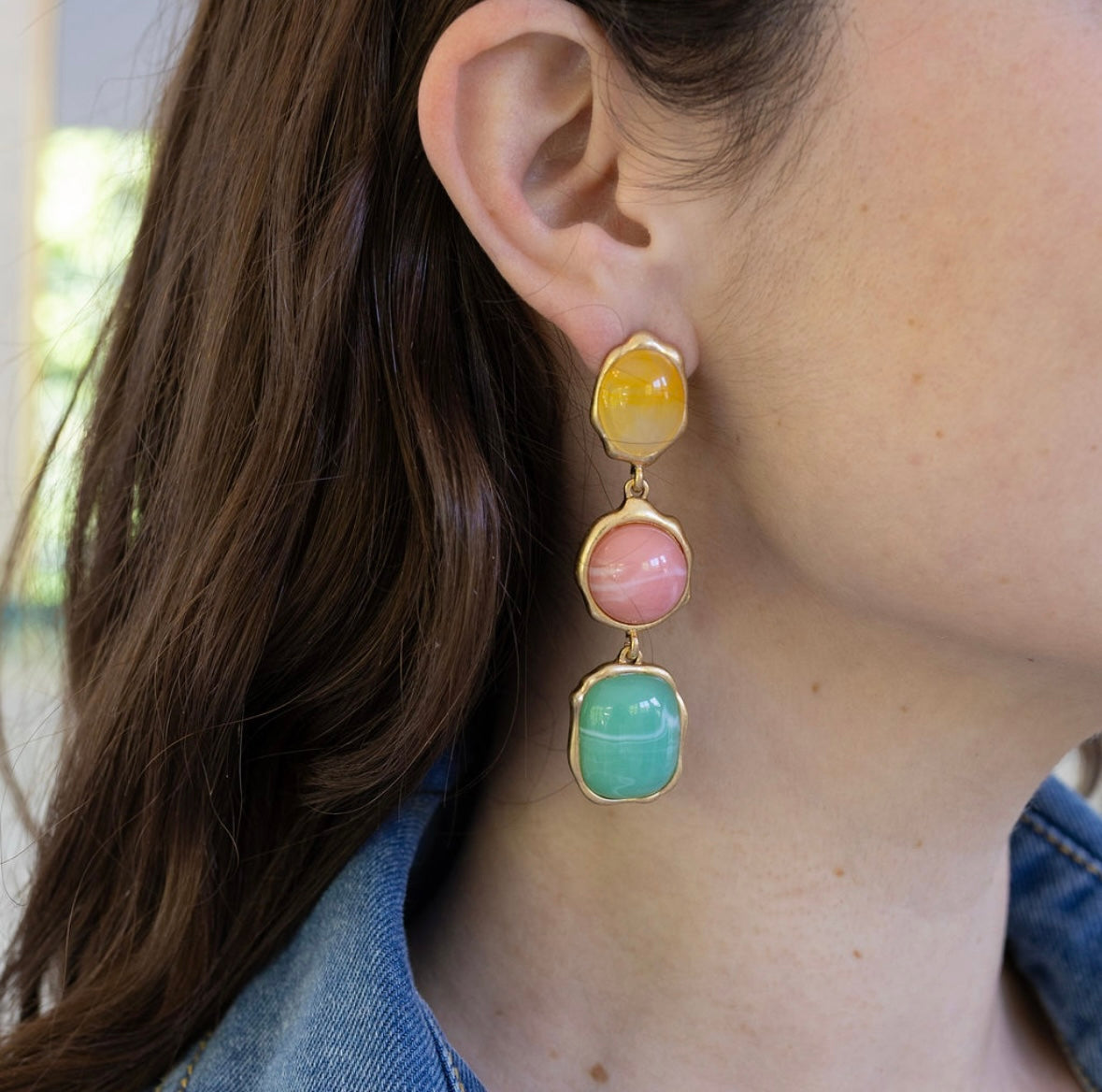 Close-up of a person wearing colorful yellow, pink, blue earrings with gold accents.