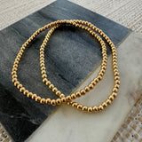 Two gold-colored stretch bracelets with bead embellishments, placed on a flat surface.