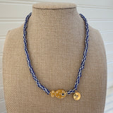 Bead necklace made of white and black striped beads with a tan polka dot fish bead at the center and a small gold disc pendant.