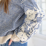 Blue and white striped sweater with lace details on cuffs and hem, worn by a person.