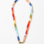 Brightly colored bead necklace with orange, yellow, blues and green beads. Necklace has a large gold clasp at its center.