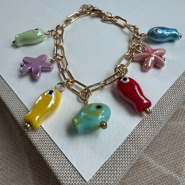 Picture of a delicate gold link chain bracelet with 5 fish beads in green, yellow, red, turquoise and blue. There are also two starfish beads that are purple and pink.