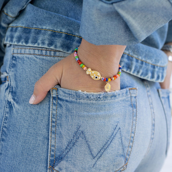 Picture of a woman's hand in her back pocket. On her wrist is a bracelet with small multicolored beads and one tan fish bead.