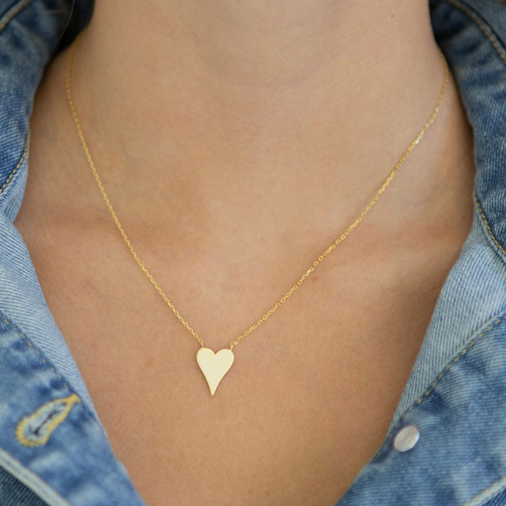 Delicate gold heart-shaped necklace on a person wearing a denim jacket.
