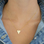 Delicate gold heart-shaped necklace on a person wearing a denim jacket.
