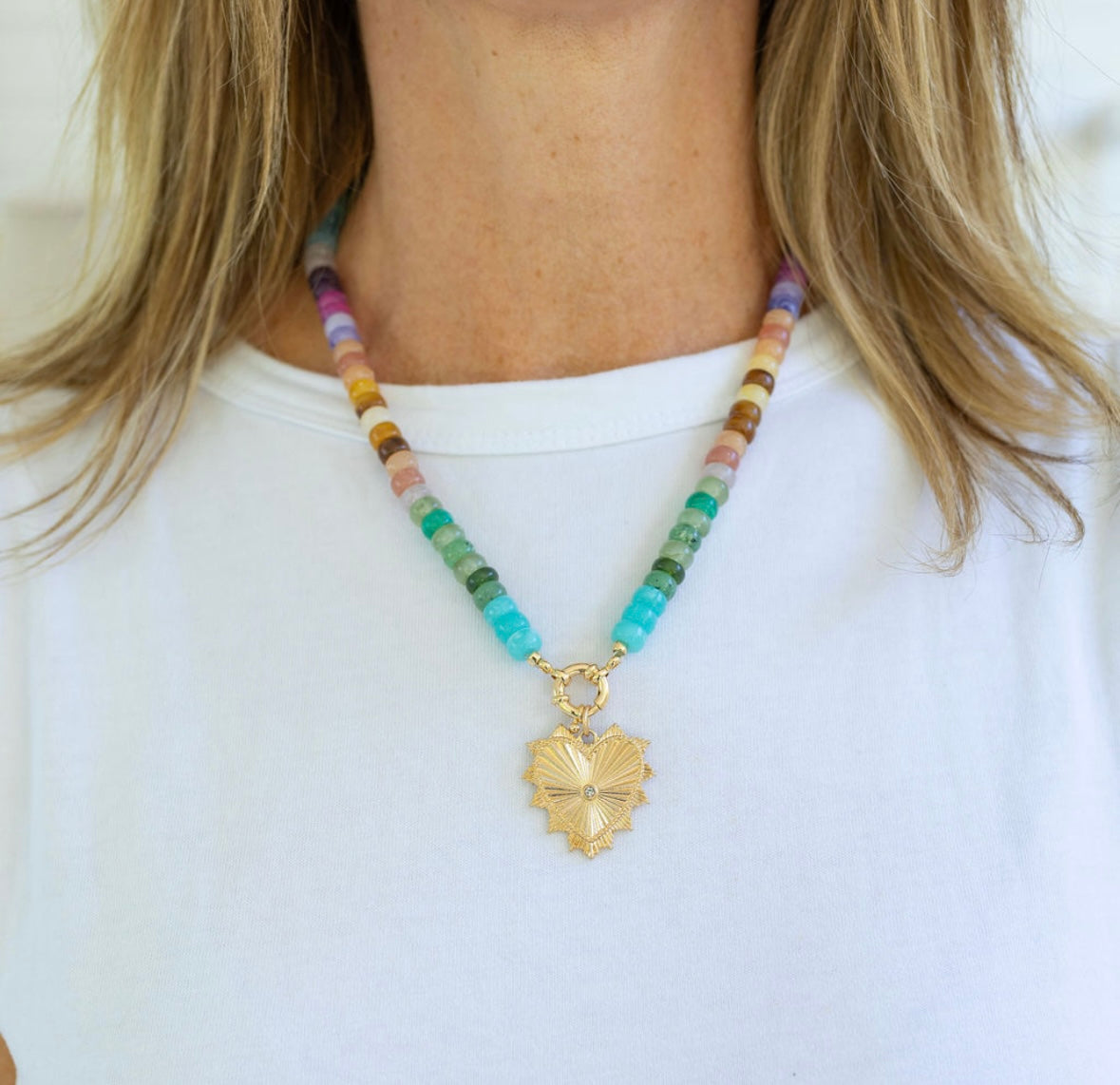 Colorful beaded necklace with a gold heart pendant worn by a person on a white background