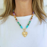 Colorful beaded necklace with a gold heart pendant worn by a person on a white background