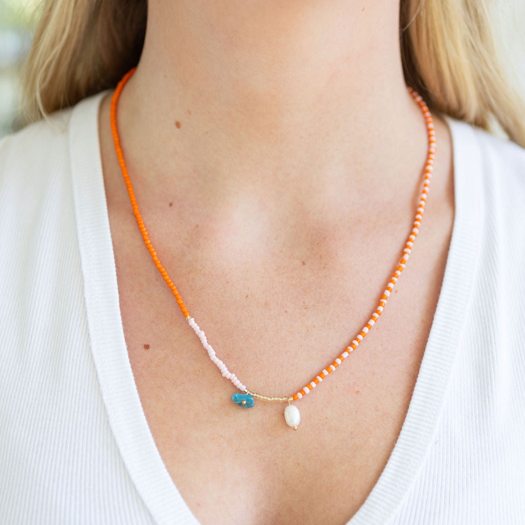 Necklace with orange beads and a blue and white pendant on a person wearing a white top.
