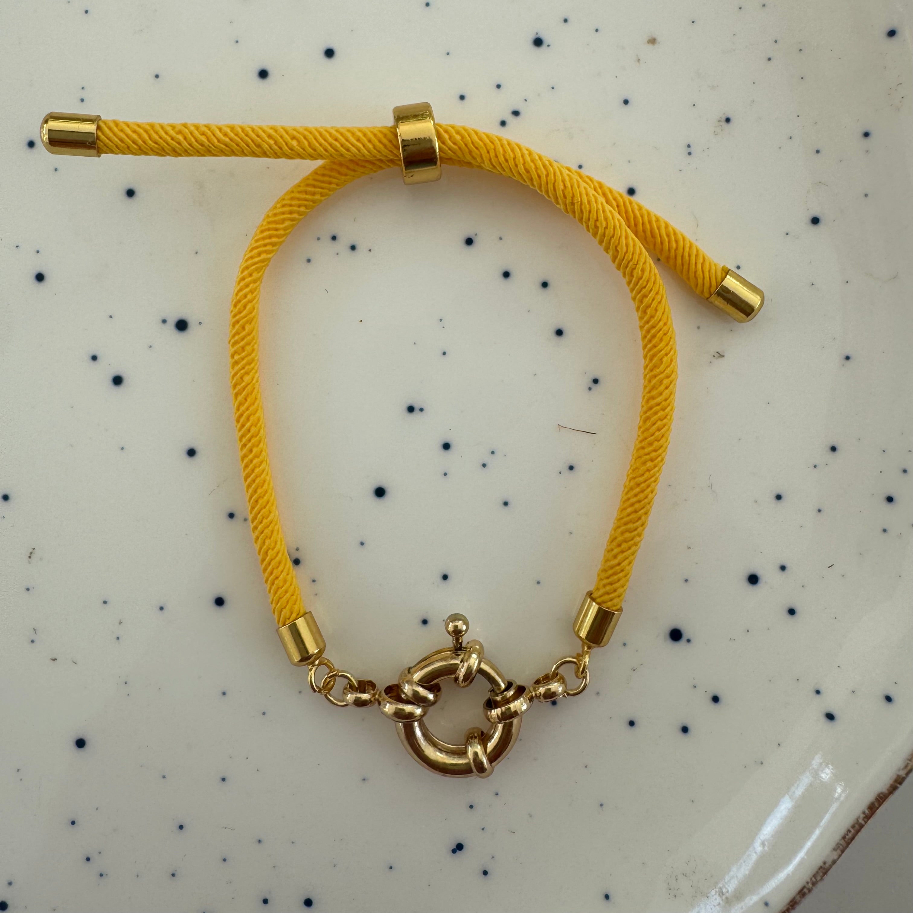 Yellow bracelet with gold clasp on a speckled surface