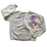 Picture of a cream colored sweater with a purple flower with a red center and red lettering that read, "Happy Vibes".