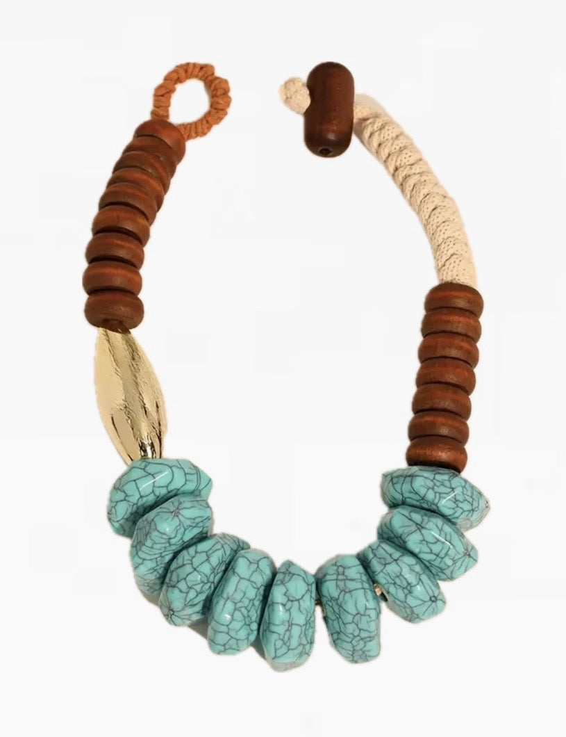 Picture of a chunky statement necklace made of natural cream cord, wood beads, turquoise beads and a large gold bead.