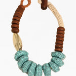 Picture of a chunky statement necklace made of natural cream cord, wood beads, turquoise beads and a large gold bead.