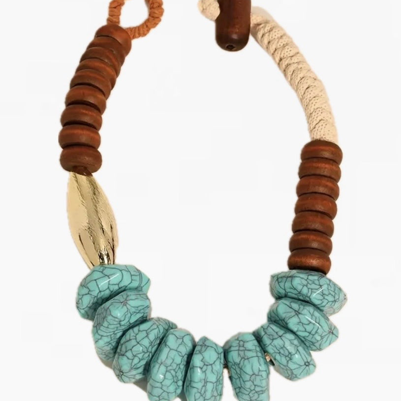 Picture of a chunky statement necklace made of natural cream cord, wood beads, turquoise beads and a large gold bead.
