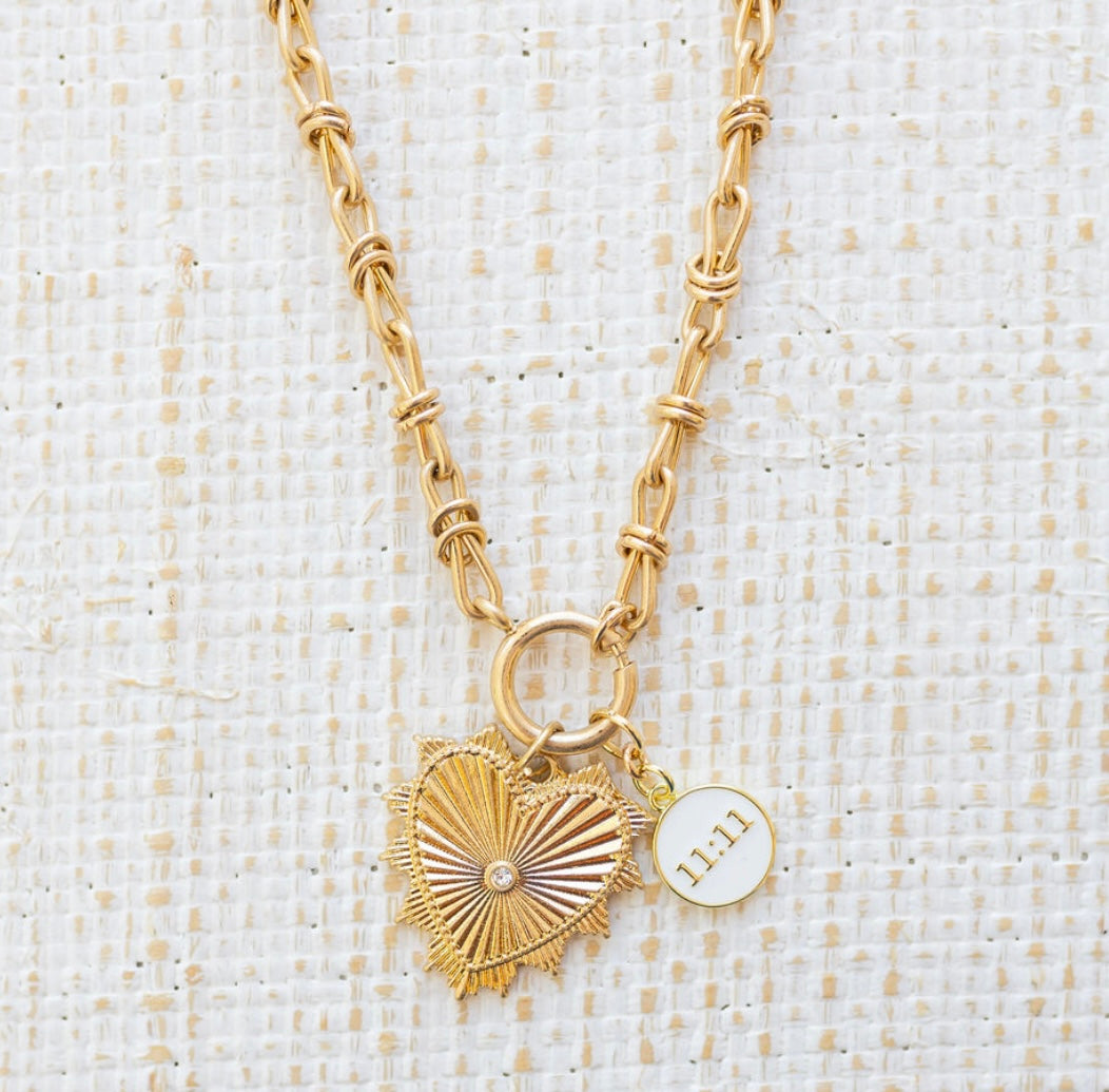 Picture of gold toggle chain with a large gold heart pendant with diamond in the center. Necklace has another white pendant that reads "11:11"