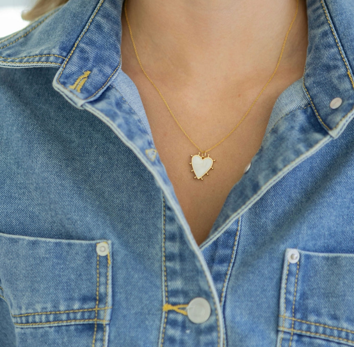 White enamel heart-shaped pendant necklace worn by a person in a denim jacket