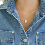 White enamel heart-shaped pendant necklace worn by a person in a denim jacket
