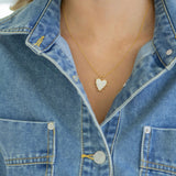 White enamel heart-shaped pendant necklace worn by a person in a denim jacket