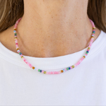 Necklace with pink and multicolored beads worn by a woman with a white Tshirt.