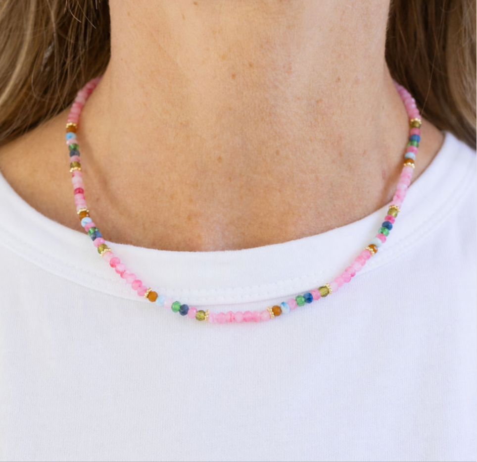 Necklace with pink and multicolored beads worn by a woman with a white Tshirt.