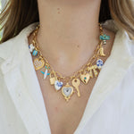 Picture of a gold charm chain necklace with 13 different charms.  Charms include a white star, gold heart, airplane, lock, heart, heart clock, key, gold heart with a blue diamond center, gold bow, ceramic white bead, Cowboy boot and palm tree.