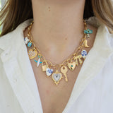 Picture of a gold charm chain necklace with 13 different charms.  Charms include a white star, gold heart, airplane, lock, heart, heart clock, key, gold heart with a blue diamond center, gold bow, ceramic white bead, Cowboy boot and palm tree.