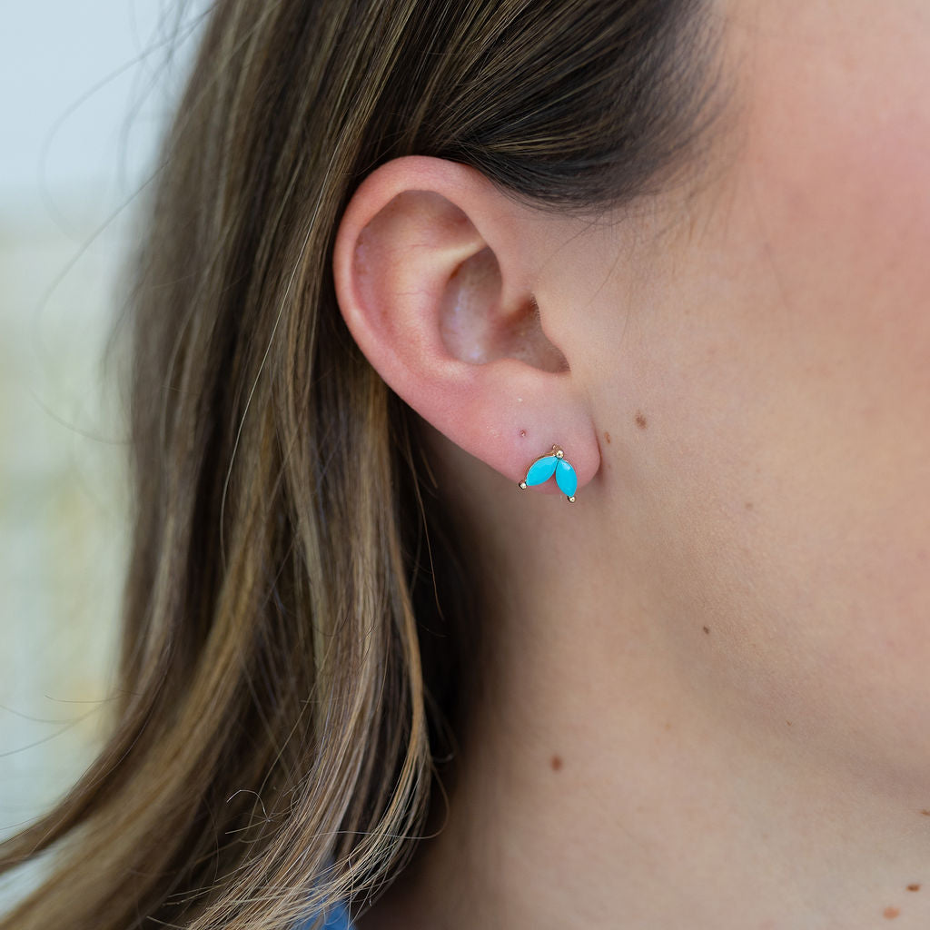 Picture of a woman's ear wearing studs made of two dainty turquoise ovals.
