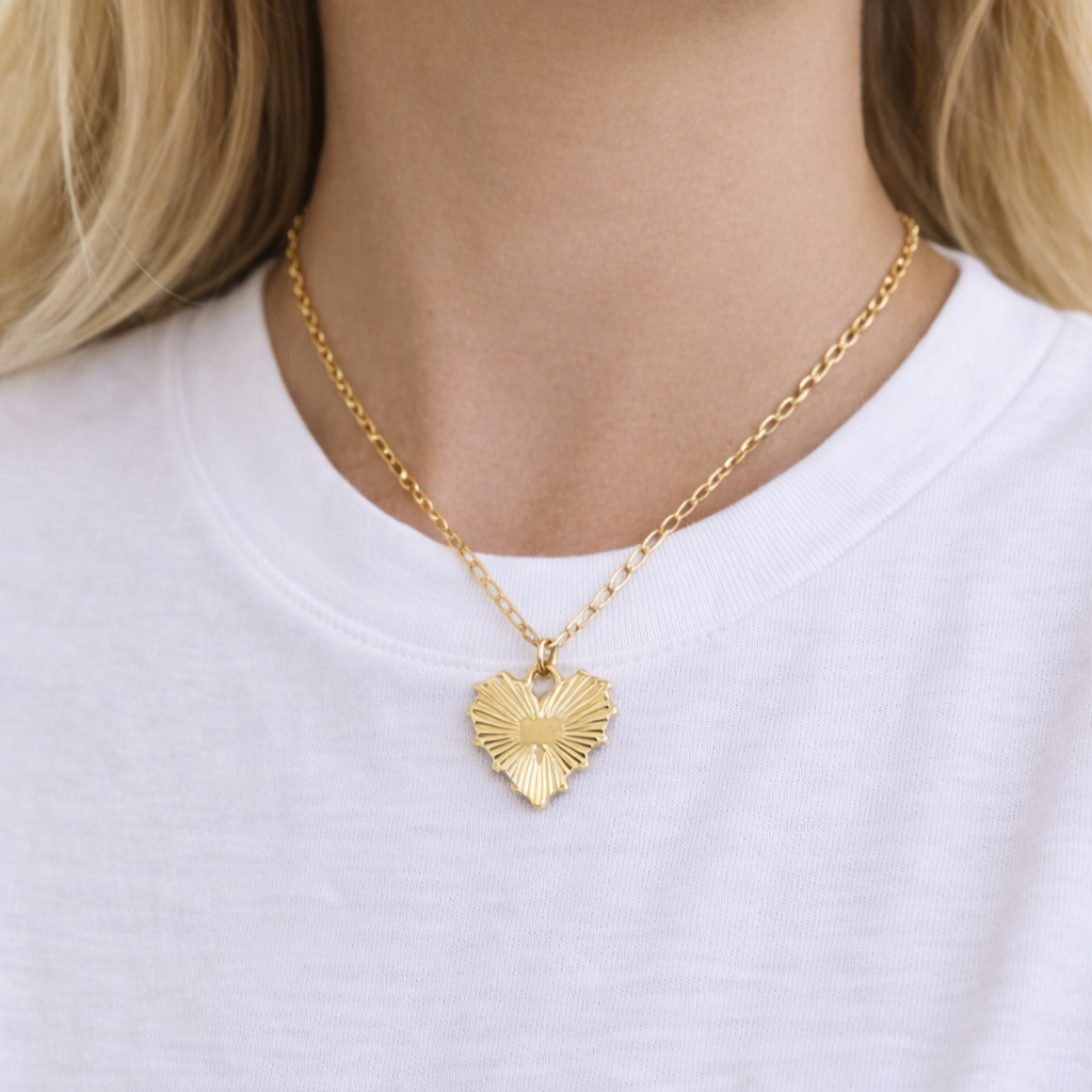 Gold heart-shaped necklace worn by a person in a white t-shirt.