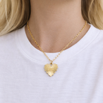 Gold heart-shaped necklace worn by a person in a white t-shirt.