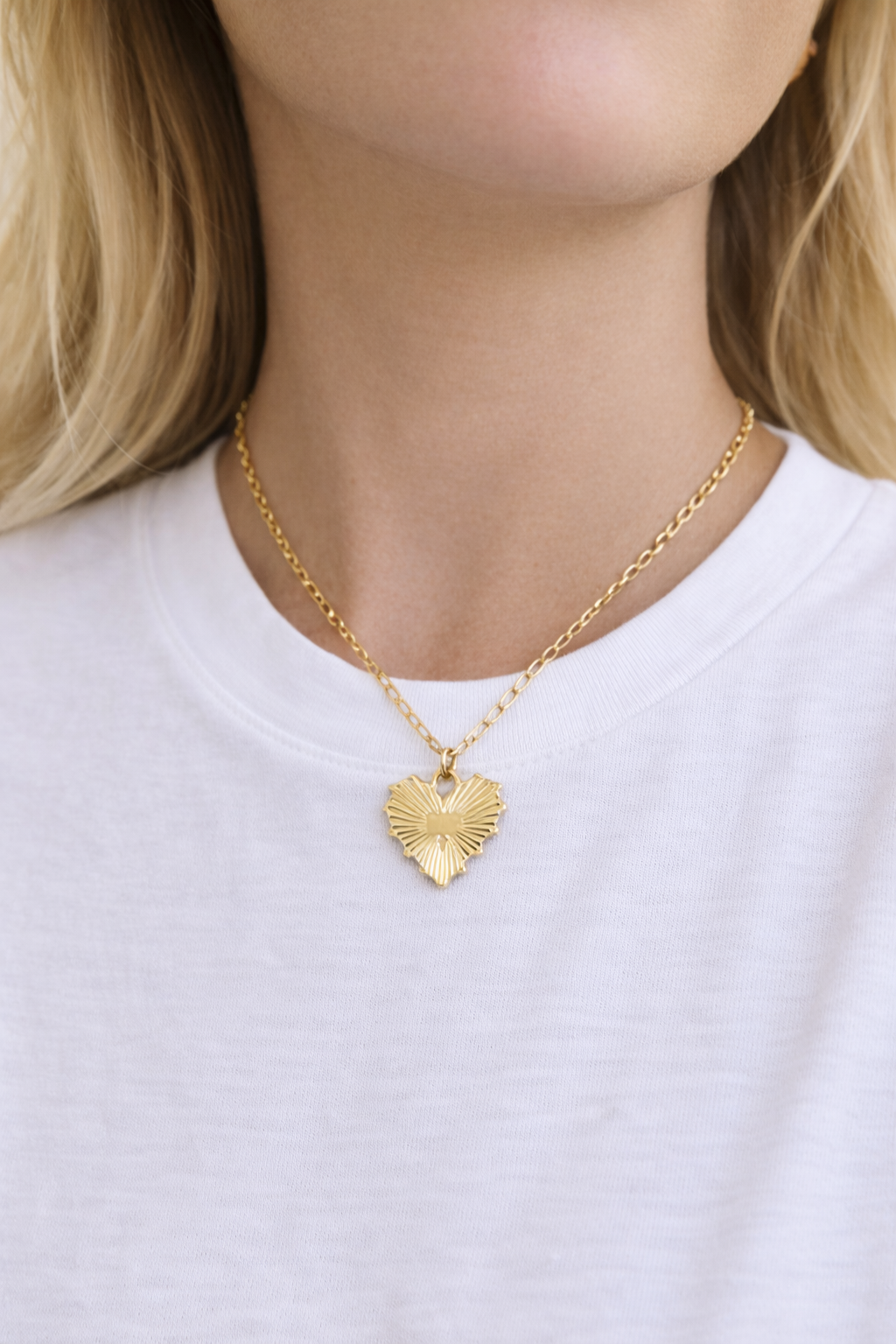 Gold heart-shaped necklace worn by a person in a white t-shirt.