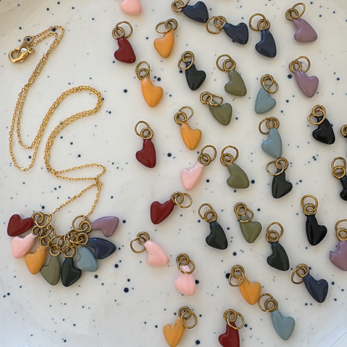 Colorful heart-shaped charms on a speckled ceramic plate with a gold necklace.