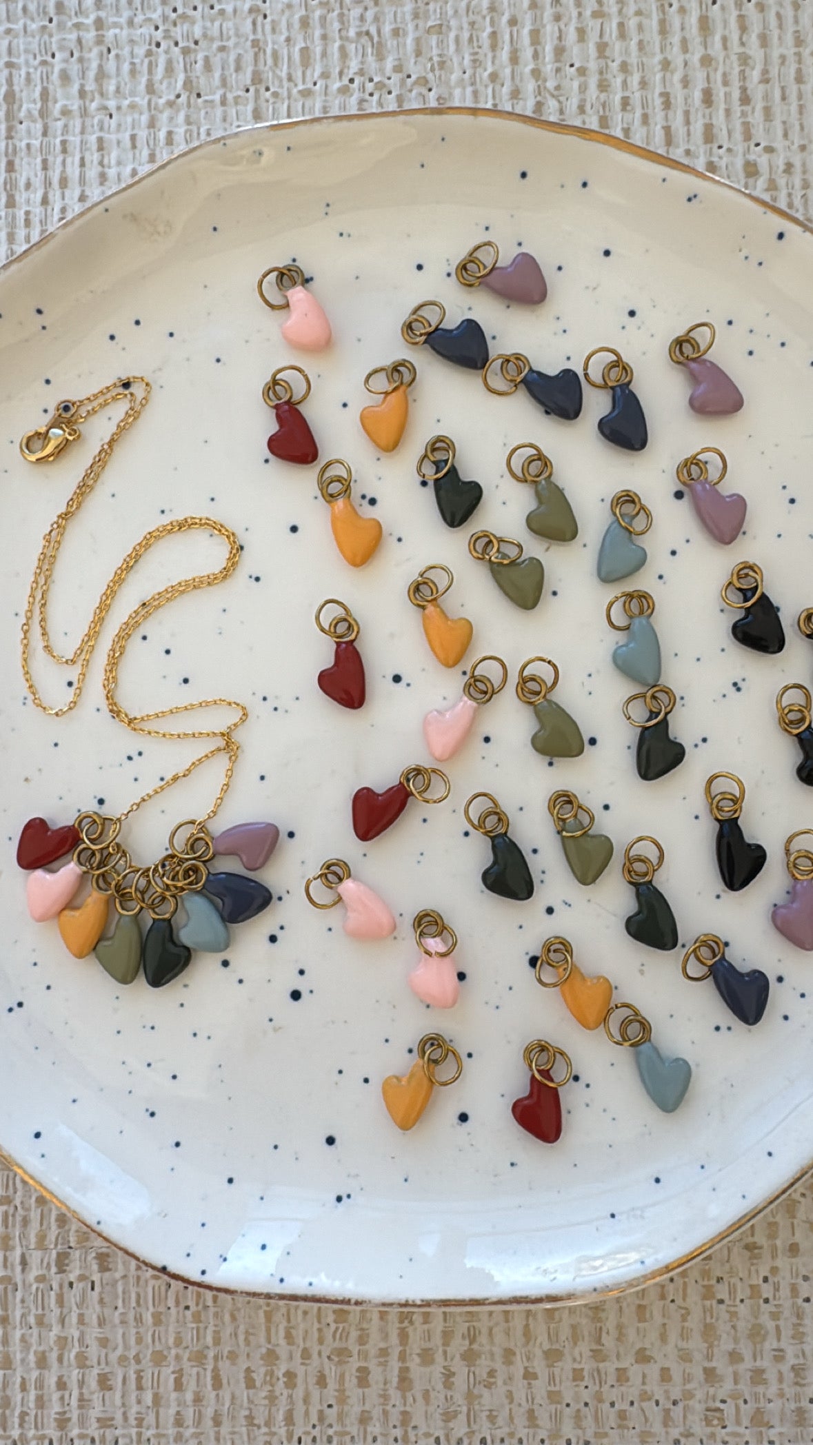 Colorful heart-shaped charms on a speckled ceramic plate with a gold necklace.